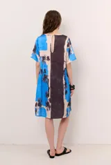 Vestido corto de corte recto y holgado, con mangas cortas y cuello redondo. Presenta un diseño estampado con motivos florales oscuros y una franja lateral en tono contrastante.