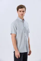 Camisa de manga corta confeccionada en mezcla de lino y algodón, con diseño de rayas verticales en tonos celeste y blanco. Cuenta con cuello camisero, botonadura frontal y bordado sutil en el pecho.