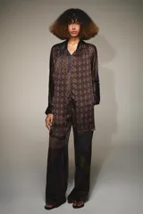 Pantalón de tiro alto confeccionado en seda, con cintura ajustable mediante cordones. Presenta un diseño de patchwork con diversos estampados geométricos y paisley en tonos tierra, verde y violeta.