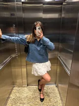 Camisa de denim azul con cuello polo, cierre frontal parcial y dos bolsillos cuadrados en el frente. Presenta un corte holgado y mangas largas.