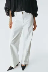 Pantalón de jean color crudo, de corte wide leg y tiro alto. Presenta cierre frontal con doble botón metálico y pliegues marcados en la parte delantera.