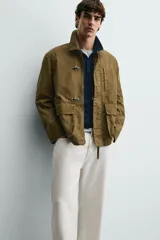 Parka de corte relajado confeccionada en mezcla de algodón color marrón. Presenta cuello solapa, cierre frontal con cremallera oculta y alamares metálicos, bolsillos de plastrón con solapa en la cadera y bolsillo de vivo en el pecho.