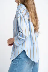 Camisa de algodón y poliamida, color celeste con rayas verticales en tono mostaza/marrón. Presenta un corte oversize, cuello clásico y mangas largas.