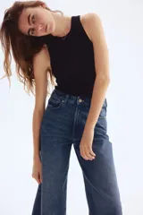 Pantalón jean azul de denim de algodón levemente elástico, corte ancho, tiro alto, largo tobillero y cinco bolsillos.