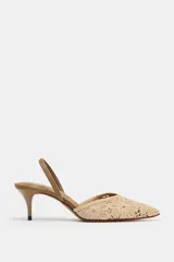 Zapato de tacón medio fino y destalonado, color beige con cuerpo de tejido bordado con motivos florales, punta fina y tira trasera elástica.