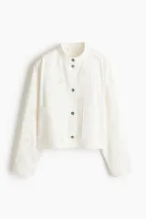 Campera corta de sarga de algodón blanca con detalles de broderie en forma de flores, cuello mao, cierre frontal con botones y bolsillos de parche delanteros.
