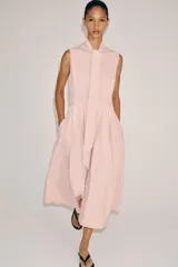 Vestido midi de Zara Woman Collection color rosado, confeccionado en hilatura de algodón. Presenta cuello subido con lazada, diseño sin mangas, bolsillos laterales ocultos y pliegues delanteros. Su falda tiene acabado en línea evasé y cuenta con cierre frontal mediante botones ocultos por solapa.