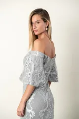 Vestido largo de fiesta color gris perla, corte sirena, con escote off-shoulder y mangas cortas con volados. Confeccionado en tul bordado con hilo al tono y leve brillo.