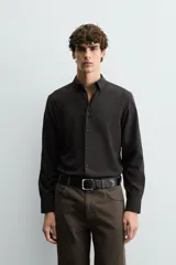 Camisa de corte slim fit, color negro, con cuello italiano, manga larga con puños abotonados y cierre frontal de botones. Confeccionada en tejido de fácil cuidado que minimiza la necesidad de planchado.