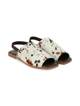 Sandalia plana Isotta de cuero con pelo, con estampado animal print tipo vaca en tonos blanco, marrón y negro. Cuenta con elástico trasero marrón y suela plana.