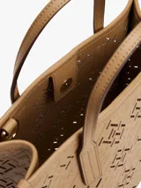 Cartera tote color beige con diseño calado del monograma TH en relieve. Tiene doble asa corta y correa larga extraíble. Incluye cierre magnético y detalles metálicos dorados.