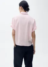 Camisa de manga corta color rosado, de diseño recto con cuello camisero y cierre frontal de botones.