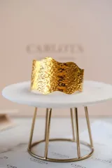 Brazalete rígido de diseño orgánico con bordes ondulados y textura martillada. Acabado en tono dorado brillante.