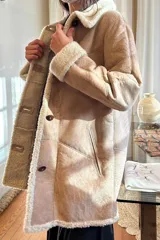 Campera tipo gamulán de cuero genuino en color marrón, con interior y detalles en corderito sintético color crema. Presenta cierre frontal con botones, cuello solapa y puños con vuelta.
