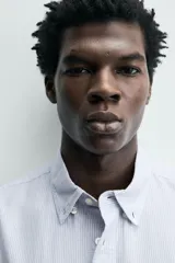 Camisa de corte regular fit confeccionada en tejido de algodón con diseño de rayas verticales. Presenta cuello abotonado, manga larga con puños abotonados, bolsillo plastrón en el pecho y cierre frontal con botones.