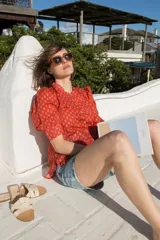 Camisa de estilo romántico color rojo con estampado floral pequeño en tono azulado, cuello redondo, cierre frontal con botones y mangas al codo con frunces en los hombros.