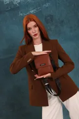 Phonebag pequeña color mostaza, confeccionada en cuero sintético, con solapa frontal y correa ajustable con logo de la marca.