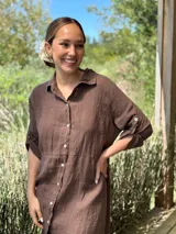 Vestido camisero largo de lino blanco, con cuello camisero, manga corta enrollada y cierre frontal de botones de nácar. Presenta aberturas laterales en el bajo.