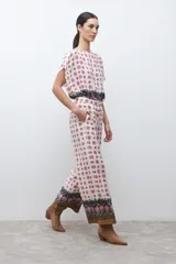 Pantalón de corte recto y tiro alto con estampado geométrico en tonos rojos y negros sobre fondo crudo. Presenta un borde inferior con diseño ornamental y bolsillos laterales.