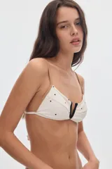 Top de bikini ajustable de color blanco crema con estampado de lunares negros, detalles de vivos en contratono camel y escote en V con ribete negro.