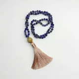 Japa mala compuesto por 108 cuentas de sodalita azul, con un dije gurú de madera y una borla de hilo de seda en color beige. El diseño incluye separadores de nudos en hilo color salmón.