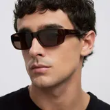 Lentes de sol con diseño rectangular y envolvente de estilo deportivo. Montura de material bio-based color mostaza con lentes polarizadas color marrón.