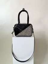 Cartera rígida negra con detalles en rojo y tachas plateadas. Tiene herrajes y cierre metálico plateado marca YKK, asa fina para llevar al hombro o en la mano y correa larga extra regulable. El interior es forrado, tiene un bolsillo con cierre enmarcado en cuero, y un segundo bolsillo plaqué.