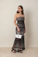 Vestido largo de fiesta negro con forro color nude y encaje calado con motivos geométricos. Diseño strapless con transparencia en cintura y ruedo.