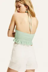 Top corto verde agua con textura arrugada, cuello halter con volantes y lazos para atar en la nuca, espalda descubierta y volantes en el ruedo.