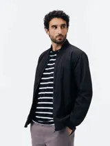 Campera bomber negra con cierre frontal, cuello, puños y dobladillo en rib elástico, y bolsillos laterales.