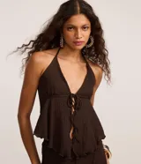 Blusa beige texturizada de corte halter con escote en V, lazo frontal ajustable en el busto y ruedo asimétrico ondulado.
