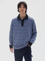 Chomba de manga larga con diseño de rayas horizontales en tonos azules y marrones, con efecto lavado. Presenta cuello polo y cartera de botones en color negro, además de puños negros y bordado pequeño en el pecho.
