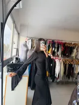 Vestido largo negro de corte ajustado, con mangas largas acampanadas y detalle de nudo frontal en la cintura que crea un efecto drapeado.