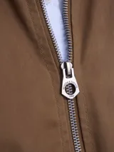 Campera tipo bomber color marrón, confeccionada en tela encerada, con cierre frontal, cuello tipo mao y puños y ruedo acanalados.