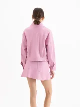 Chaqueta de cuero ovino color negro, con textura graneada, silueta de hombros caídos y largo a la cadera. Presenta recortes en el delantero y la espalda, dos bolsillos superiores con tapa y dos bolsillos laterales, cierre frontal con botones metálicos y cuello camisero.
