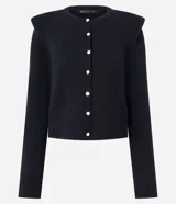 Cardigan de punto color blanco, de corte regular y ajuste al cuerpo. Presenta cuello redondo, mangas largas, cierre frontal con botones delicados y hombreras estructuradas que aportan volumen a la silueta.