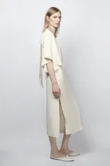 Vestido midi fluido de cuello alto y manga corta tipo capa. Presenta un diseño minimalista con bajo recto y aberturas laterales, con cierre en la espalda.