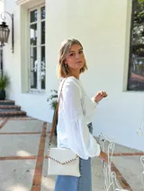 Cartera tipo sobre color crudo, confeccionada en cuero, con correa larga de cuero marrón y costuras decorativas en contraste.