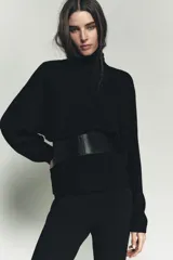 Jersey de punto liso color negro, con cuello subido y mangas largas de diseño murciélago con sisa ancha que se estrecha hacia la muñeca.