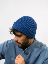Gorro tipo beanie de tejido acanalado en color azul, con parche rectangular rojo en el frente que presenta el logo de la marca Umbro bordado en blanco.