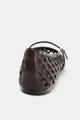 Zapato plano tipo bailarina color marrón oscuro, con capellada trenzada, tira delantera con hebilla metálica y punta redonda.