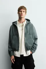 Cazadora negra de algodón con efecto lavado, corte relajado y capucha ajustable. Presenta cierre frontal de cremallera, bolsillos frontales tipo canguro y elásticos en puños y bajo.