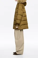 Campera puffer de largo medio en tejido técnico color verde oliva, con cierre frontal de cremallera y botones a presión. Cuenta con capucha con borde de pelo sintético desmontable, bolsillos laterales con cremallera y puños tejidos ajustados.