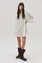 Vestido corto color crudo con rayas verticales plateadas, de manga larga abullonada y abotonado desde el escote hasta el bajo.