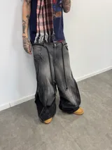 Jean de corte amplio en color negro con efecto acid wash. Presenta cierres laterales metálicos que permiten ajustar la silueta entre corte recto, oxford o baggy. Incluye una estampa gráfica de gran tamaño en la parte trasera con detalles bordados, bolsillos amplios y una etiqueta de cuero legítimo en la cintura.