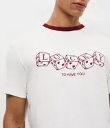 Pijama largo para hombre compuesto por una remera de manga corta blanca con cuello redondo bordó y estampa frontal de dados con la leyenda 'Lucky to Have You', y un pantalón largo blanco con estampado full print de corazones bordós y cintura elástica.