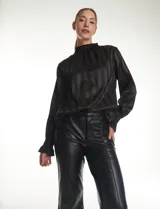 Blusa de satén negro con diseño de rayas verticales tono sobre tono. Presenta cuello alto con detalle de fruncido tipo smock, mangas largas con puños elásticos y terminación con volado.