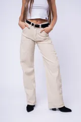 Pantalón de corte baggy color beige, de tiro medio, con bolsillos laterales y costuras verticales decorativas en las piernas.