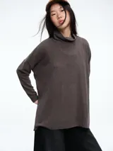 Buzo tejido de silueta holgada en color marrón, con cuello alto tipo polera, mangas largas y tajos laterales en el ruedo.