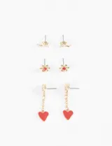 Set de tres pares de caravanas doradas con diseños variados: un par con forma de caracol con cristal, un par con forma de flor con centro rojo y un par colgante con forma de corazón rojo.